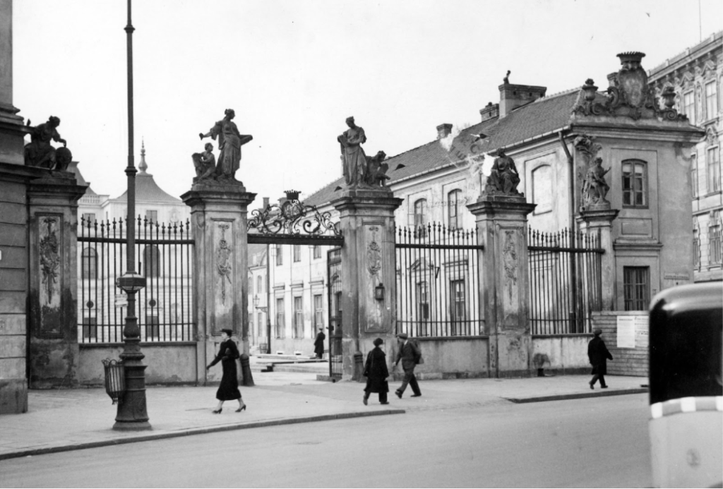 Żelazna brama Pałacu Brühla z czasów Becka, widok od zewnątrz. U góry zwieńczona alegorycznymi rzeźbami. Za bramą zarys oficyny pałacu, a w głębi jego fasada.