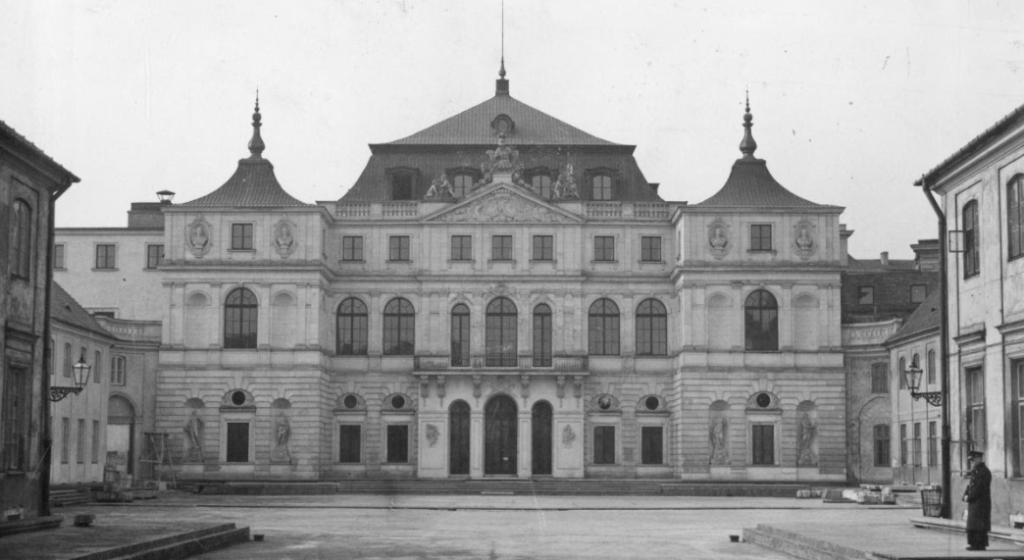 Czarno-białe zdjęcie fasady dwupiętrowego pałacyku z ozdobnym wejściem.