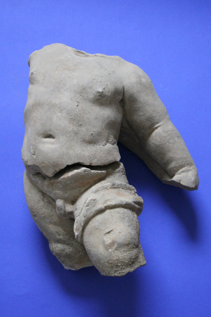 Fragmenty barokowego putto - widoczne uda, brzuch oraz ramię i przedramię. Tło błękitne.