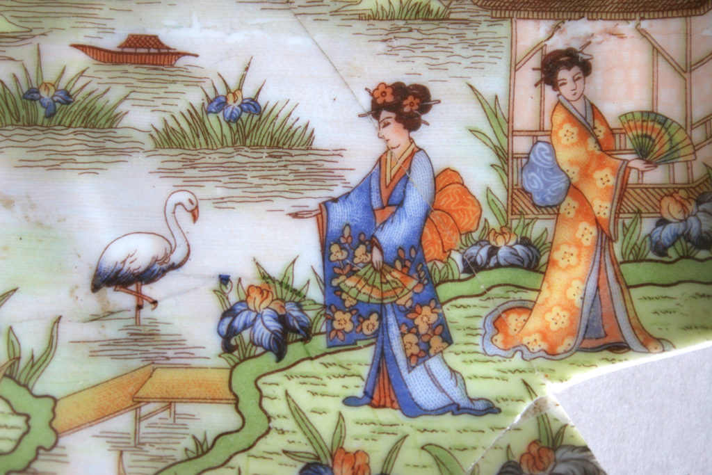 Dekoracja spodka przedstawiająca kobiety z wachlarzami w japońskich strojach. W tle woda z wyrastającymi z niej trawami i kwiatami. Kobieta na pierwszym planie prawą rękę wyciąga w kierunku bociana stojącego w wodzie na jednej nodze.