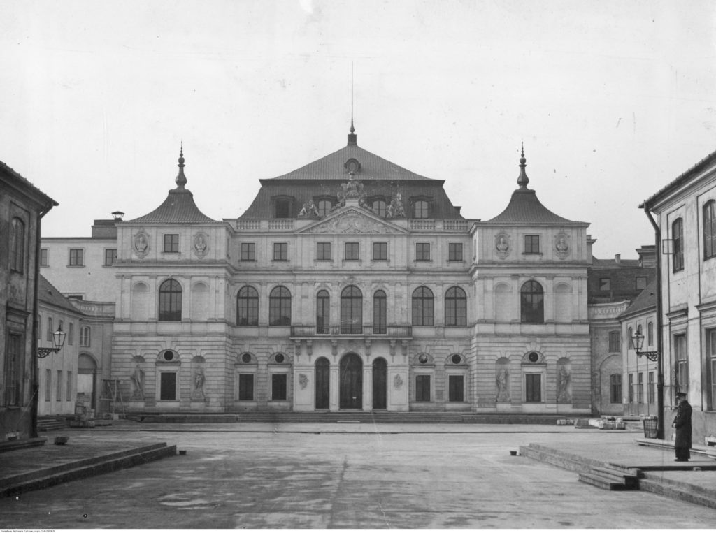 An archival photo of the facade of the Bruhl Palace. It is a highly ornamental building with two floors and a mansard roof above its corpus. There is a courtyard in front of it, surrounded on two sides by the outhouses of the palace.