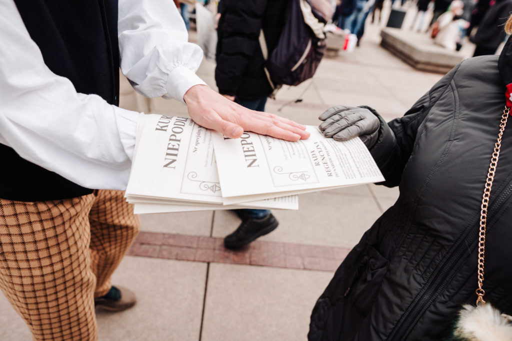 Zbliżenie na ręce mężczyzny rozdającego gazetę na ulicy.