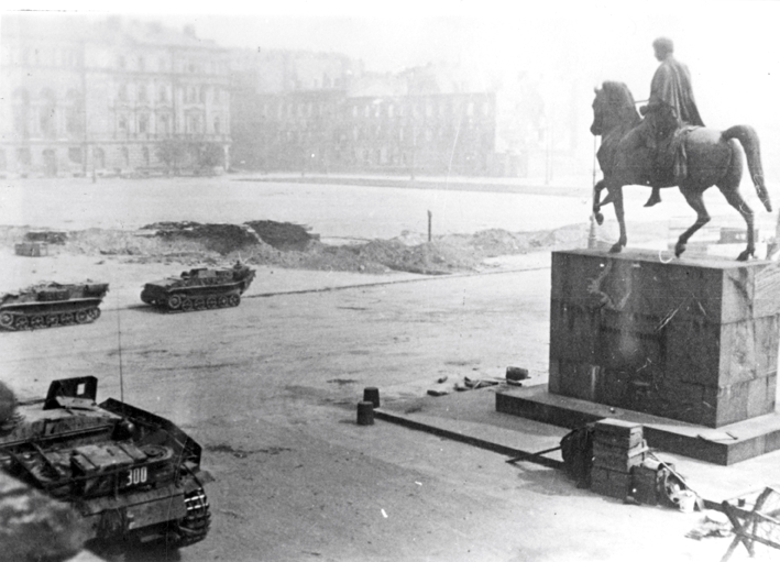 Widok na plac Piłsudskiego, po prawej stronie pomnik księcia Józefa Poniatowskiego na koniu, po lewej pojazdy pancerne, widoczne okopy.