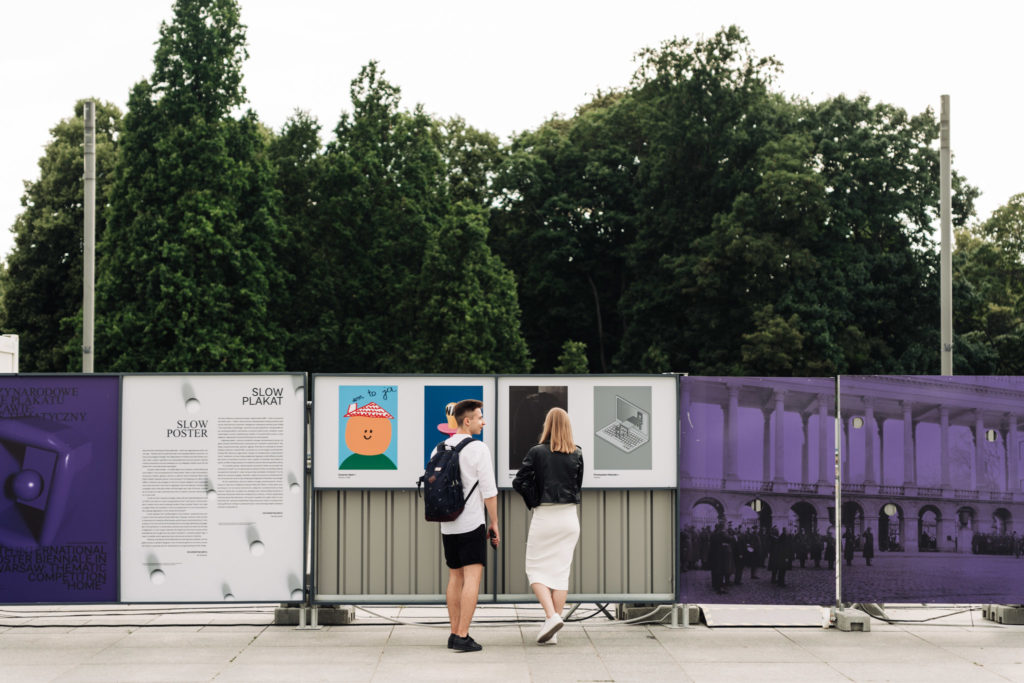 Dwoje ludzi oglądających plakaty zaprezentowane w ramach wystawy Dom na placu Piłsudskiego, podczas Biennale Plakatu.