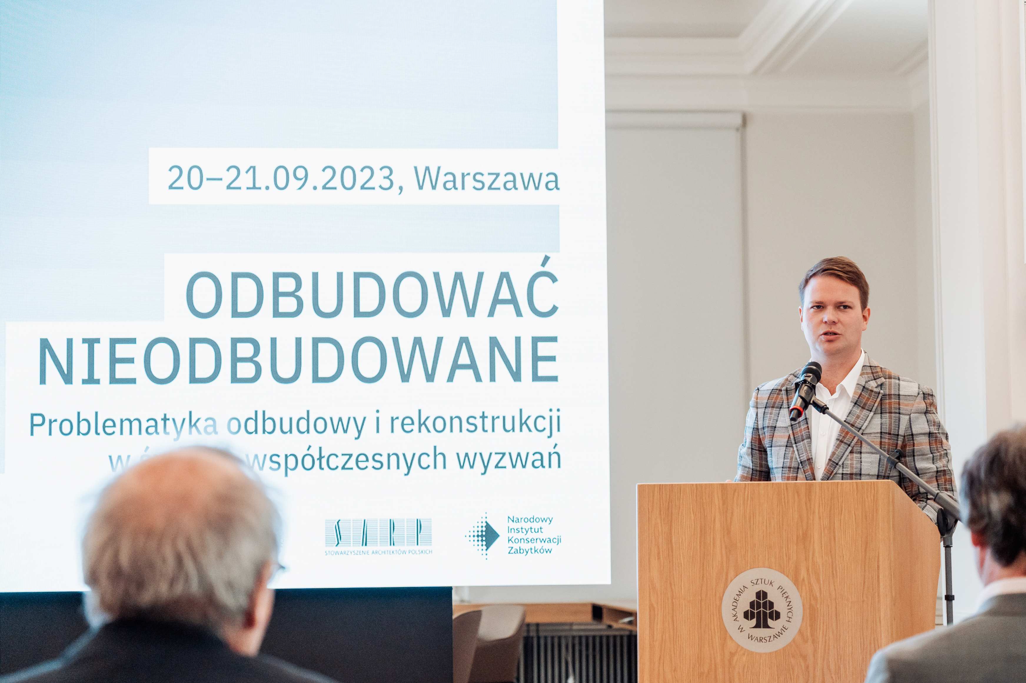 Prezes Jan Kowalski otwiera konferencję Odbudować nieodbudowane. W tle ekran z tytułem konferencji.