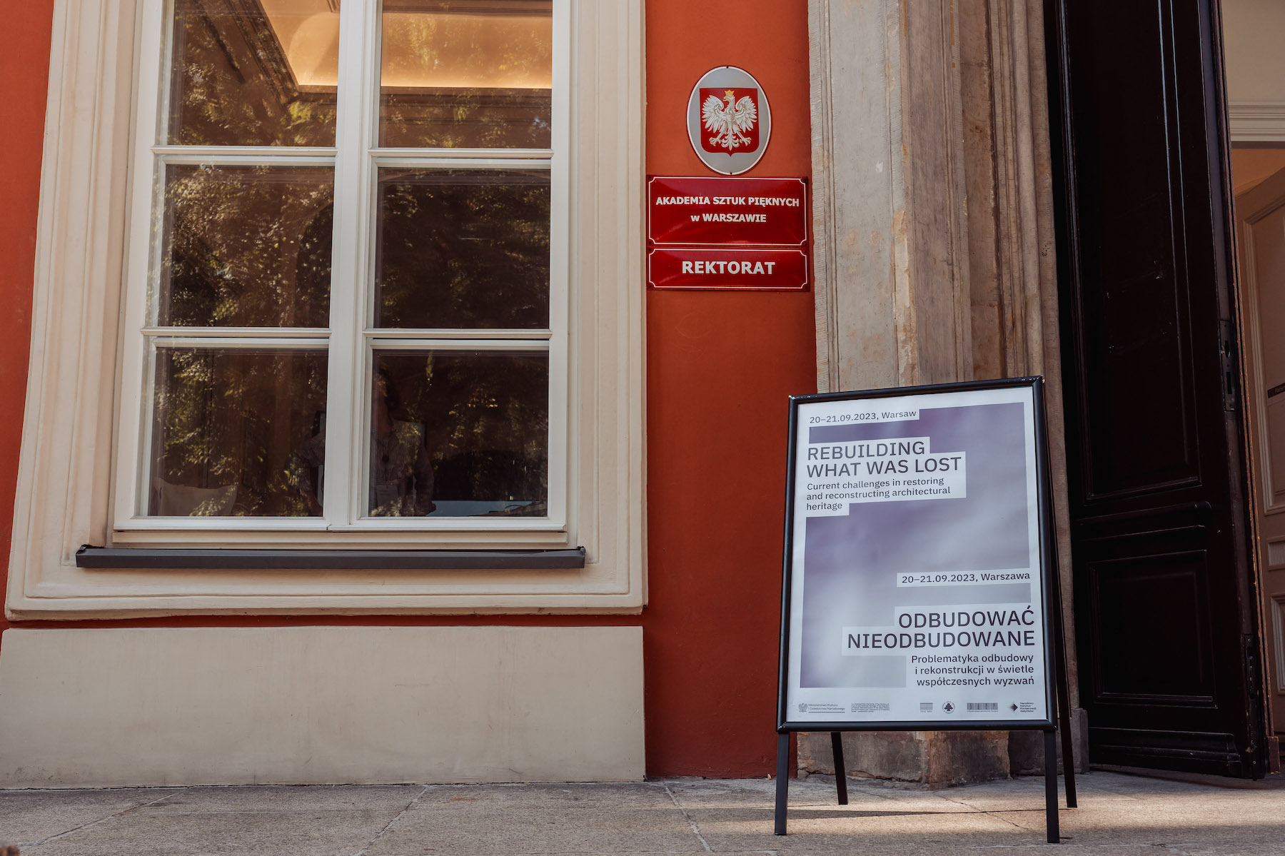 Plakat konferencji Odbudować Nieodbudowane przy wejściu do Akademii Sztuk Pięknych w Warszawie.