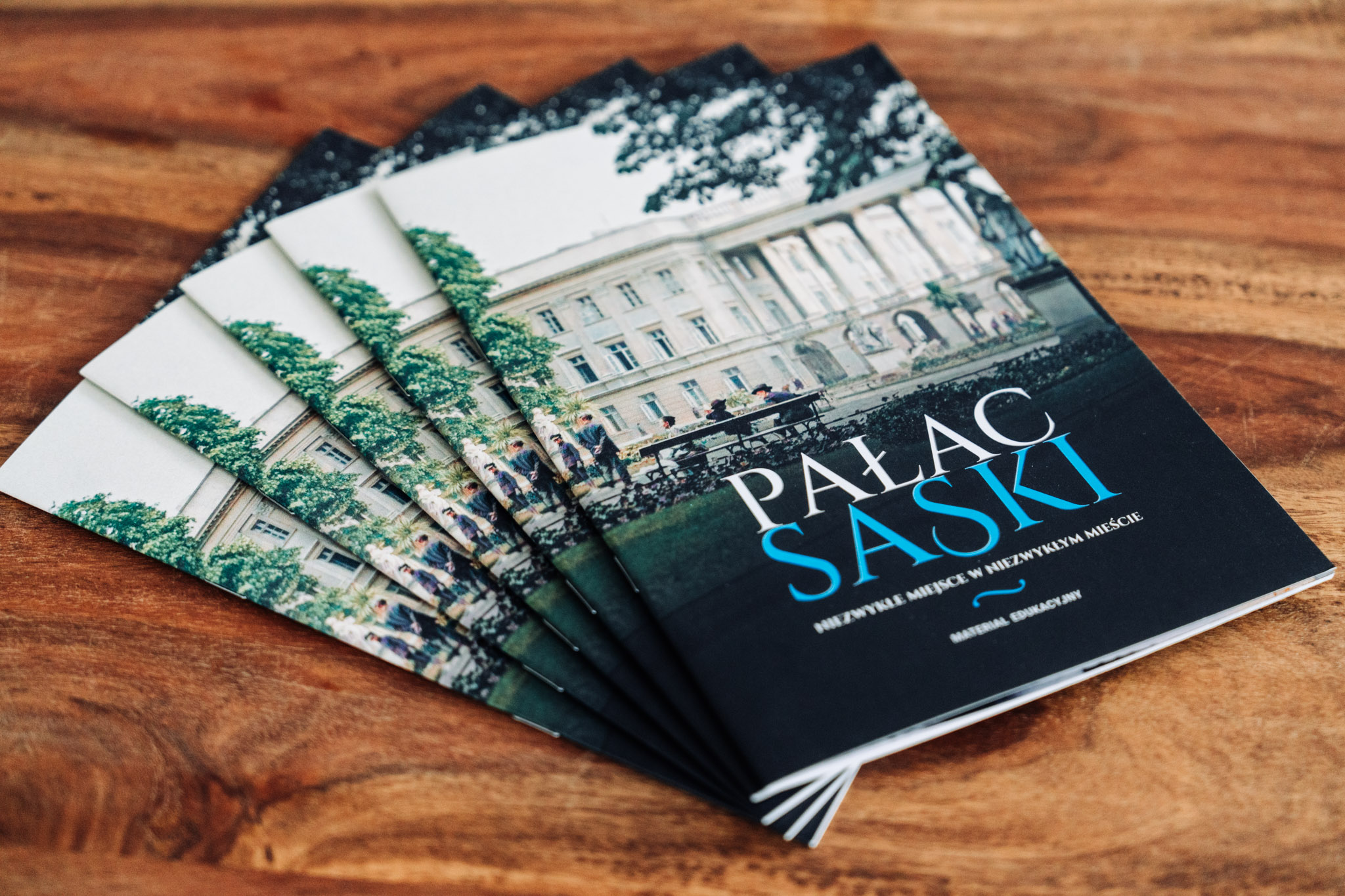 Pięć broszur edukacyjnych o Pałacu Saskim ułożonych w wachlarz. W tle drewniany blat stołu.