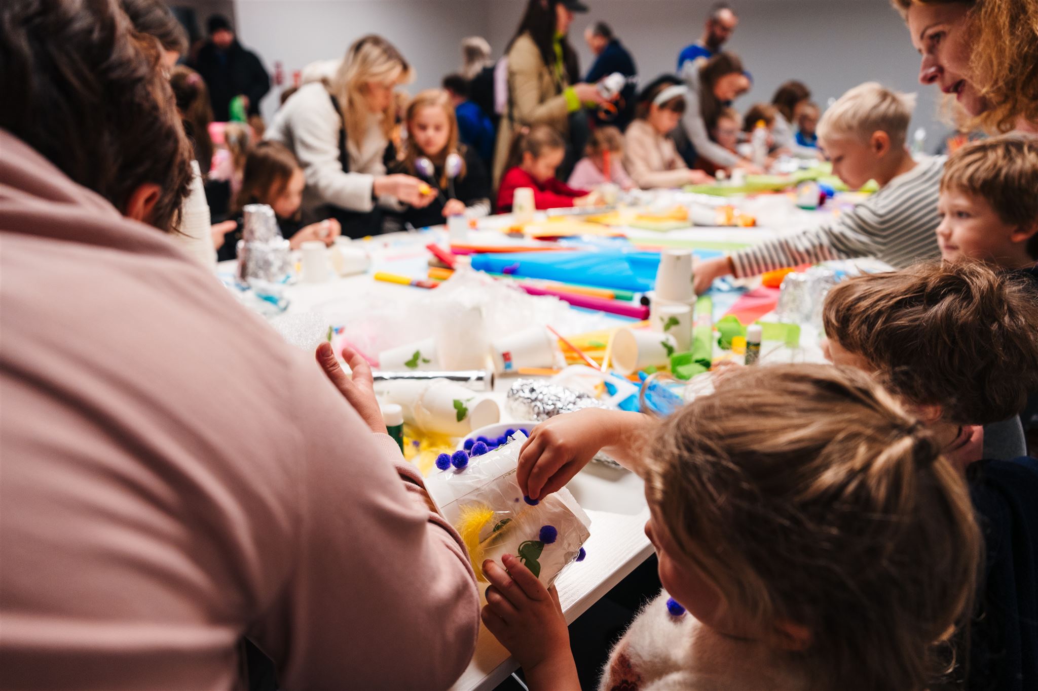 Zdjęcie wielkiego stołu zastawionego materiałami papierniczymi. Przy stole siedzą dzieci, które uczestniczą w warsztatach plastycznych podczas Festiwalu Niepodległa na Krakowskim Przedmieściu.