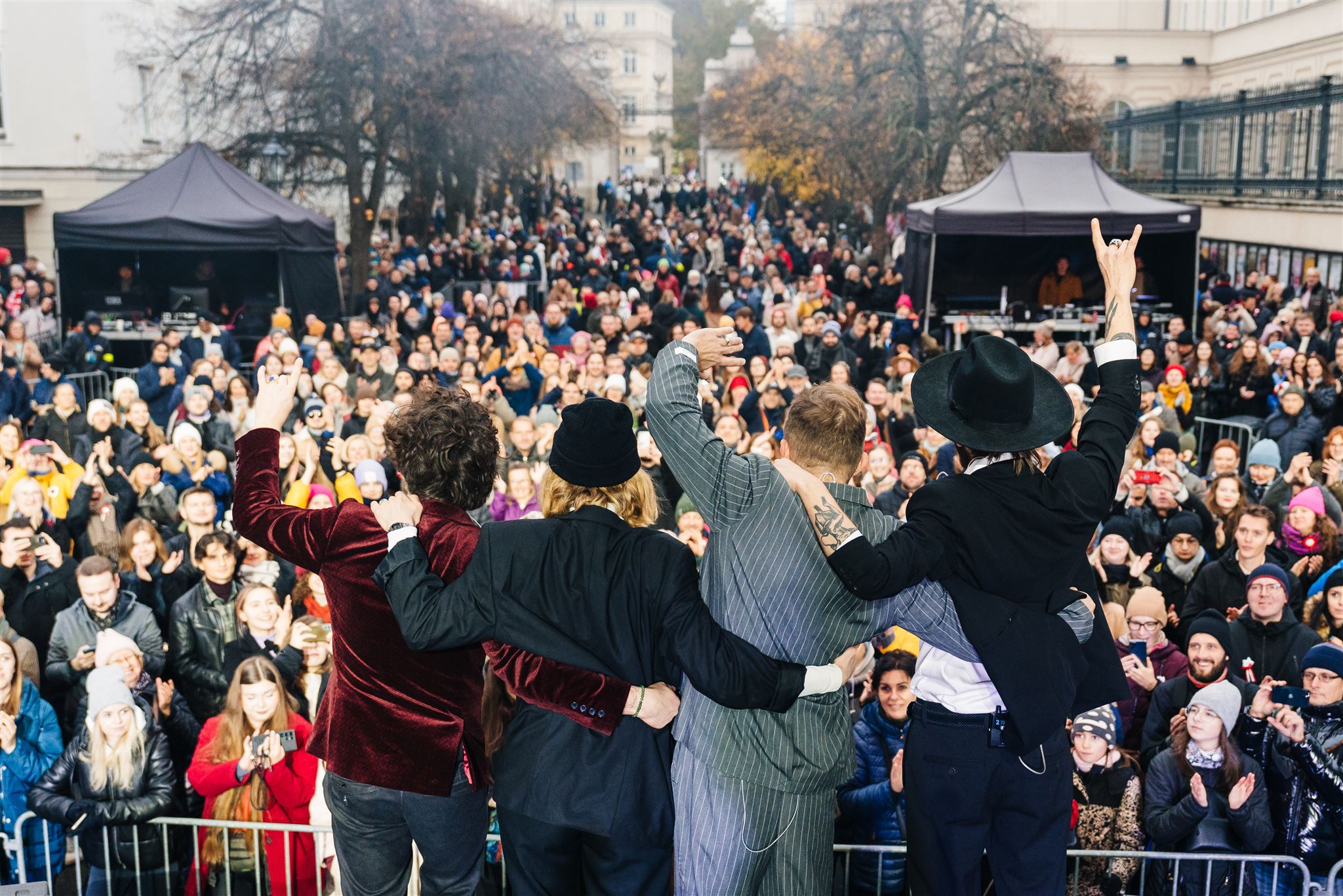 Ujęcie zza pleców czterech artystów żegnających się ze sceny z tłumem słuchających podczas Festiwalu Niepodległa na Krakowskim Przedmieściu.
