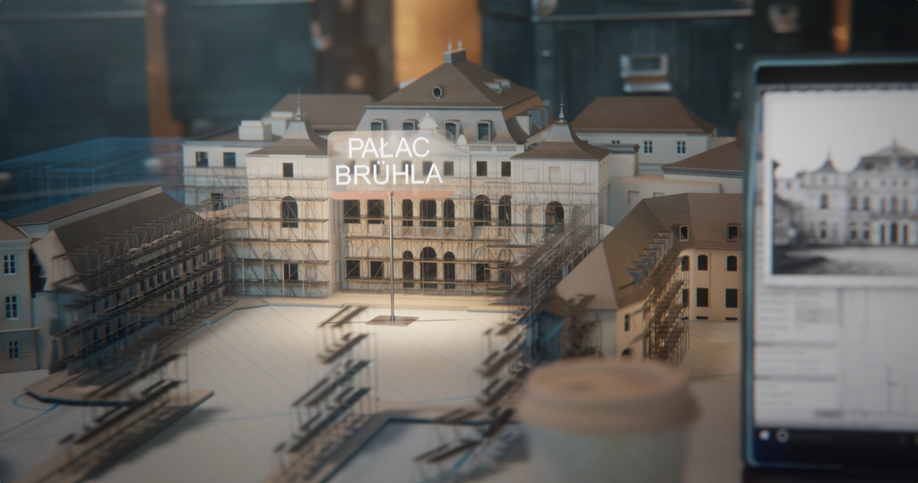 Kadr ze spotu Fototeka Pałacu Saskiego przedstawiający komputerowo zrobiony model odbudowywanego Pałacu Bruhla. Z boku kadru jest telefon komórkowy, na ekranie którego widać archiwalne zdjęcie Pałacu Bruhla.