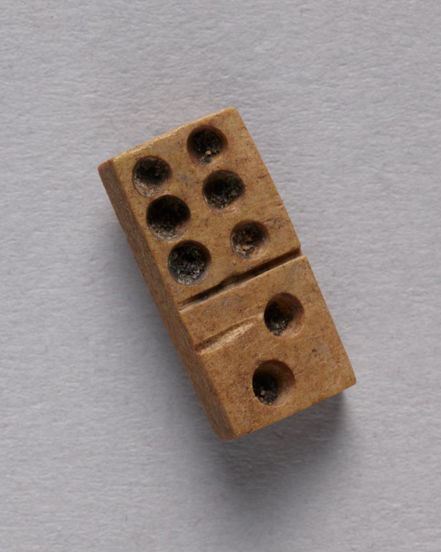 Zbliżenie na kostkę do gry w domino zrobioną z kości. Z jednej strony ma sześć oczek, czyli małych wgłębień, z drugiej dwa.