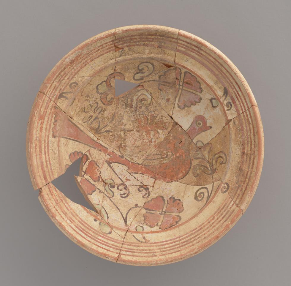 Uszkodzona misa ceramiczna sklejona ze znalezionych przez archeologów ułamków. namalowany prosty motyw roślinny otacza ptaka na środku misy.