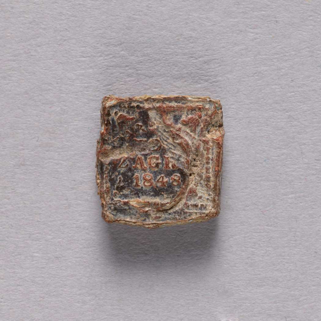 Ołowiana plomba z widoczną częściowo inskrypcją "ZAGR 1848". Kształt nieregularny, bliski kwadratowi.