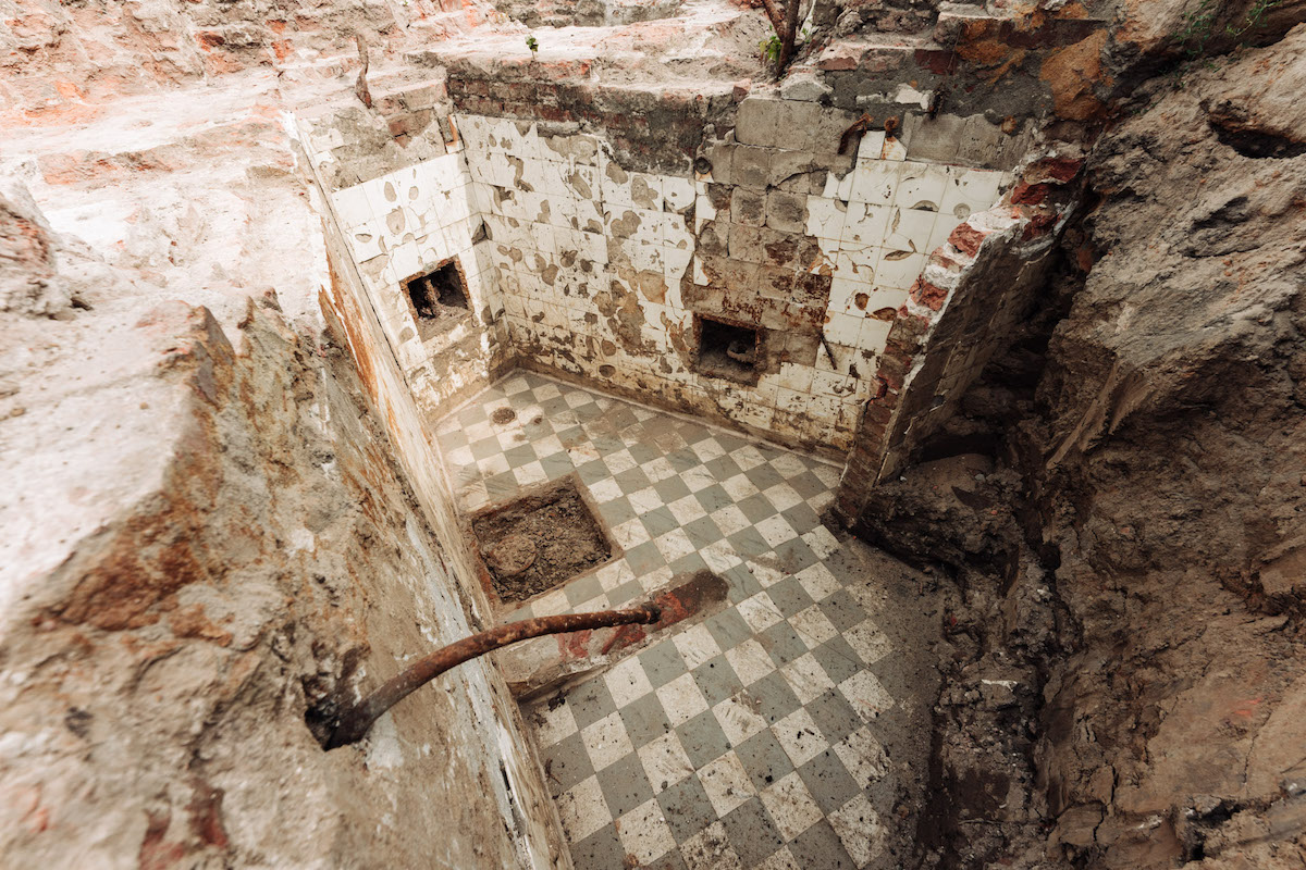 Zdjęcie pokazuje badania archeologiczne Pałacu Brühla. Na pierwszym planie w dole są pozostałości łazienki, która ma ściany i podłogę pokryte kafelkami.