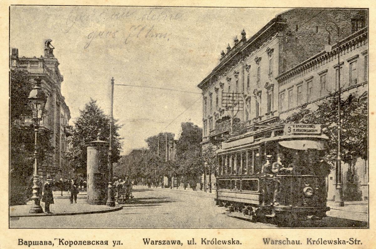 Pocztówka z ulicą Królewską. Po prawej trzypiętrowa kamienica Lessla, częściowo zasłonięta tramwajem. W tle, za kamienicą, znajdują się drzewa Ogrodu Saskiego. 