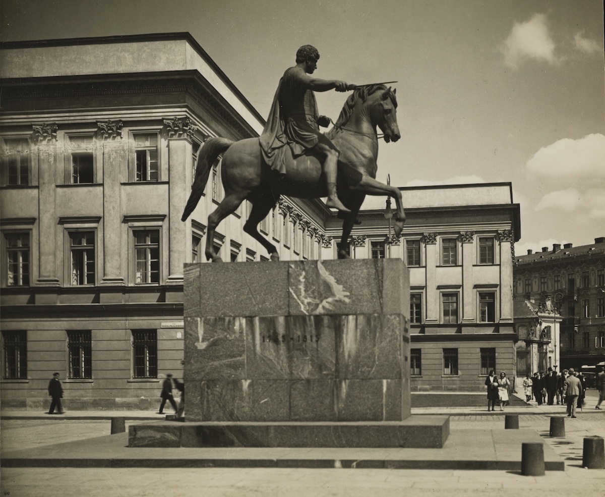 Pomnik księcia Józefa Poniatowskiego widziany z boku. Na cokole stoi koń, na którym siedzi mężczyzna ubrany w antyczny strój. W tle fragment skrzydła neoklasycystycznego Pałacu Saskiego.