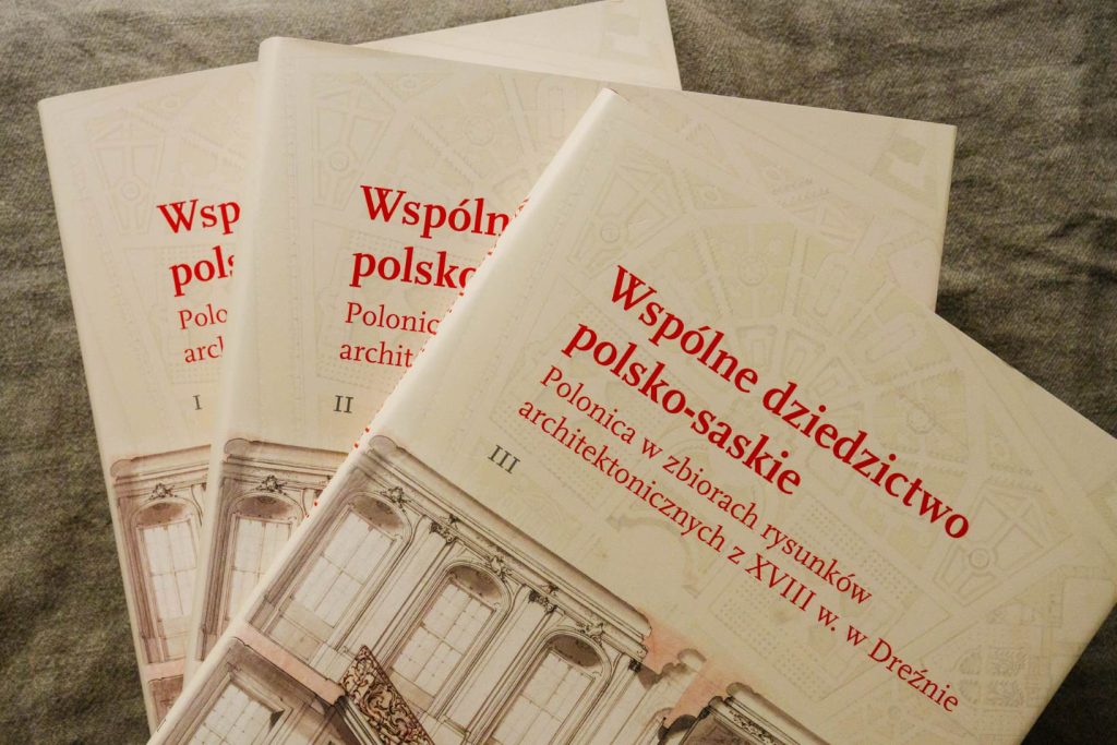 Ułożone na sobie ukośnie trzy tomy publikacji "Wspólne dziedzictwo polsko-saskie. Polonica w zbiorach rysunków architektonicznych z XVIII w. w Dreźnie" na tle lnianego materiału.