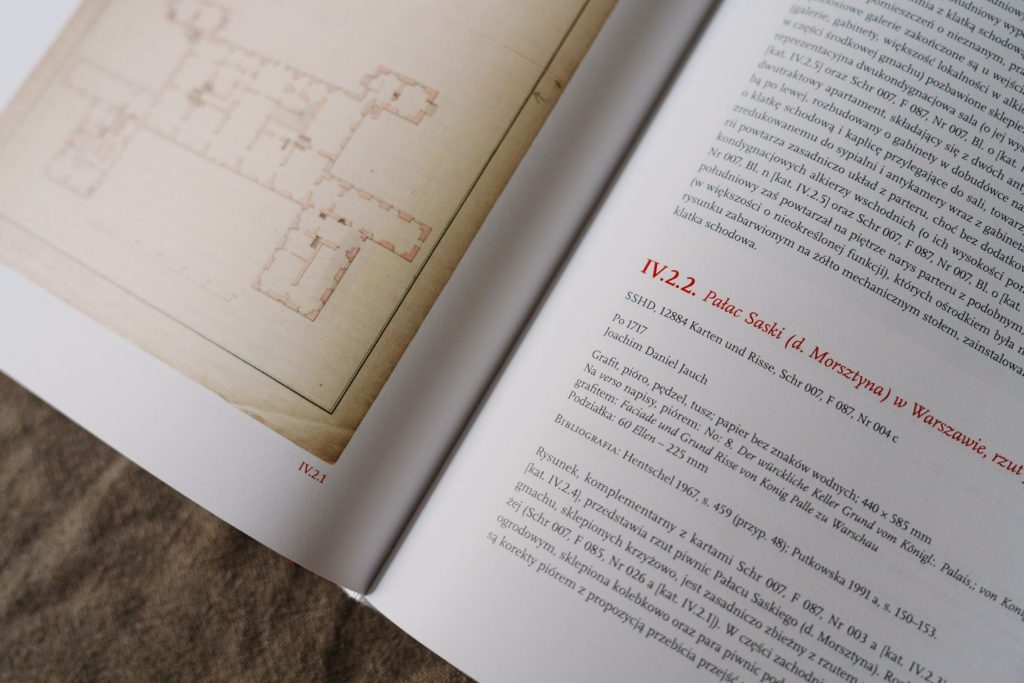 Ujęcie z ukosa fragmentu publikacji "Wspólne dziedzictwo polsko-saskie. Polonica w zbiorach rysunków architektonicznych z XVIII w. w Dreźnie" na tle lnianego materiału. Na stronie po lewej dawny plan architektoniczny w odcieniu beżu i brązu, na stronie po prawej tekst, w tym tytuł podrozdziału: IV.2.2. Pałac Saski (d. Morsztyna) w Warszawie.