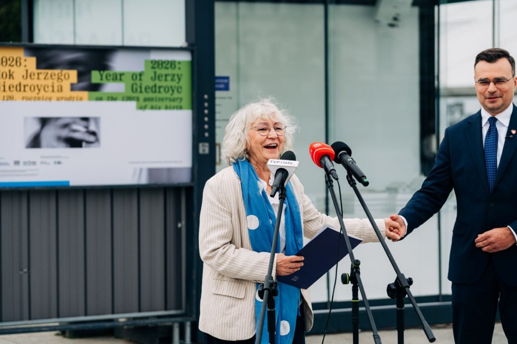 Przed mikrofonem przemawia uśmiechnięta Anna Bernhardt, prezes Stowarzyszenia Instytut Literacki KULTURA i Fundacji Kultury Paryskiej. Subtelnie za rękę trzyma ją Maciej Wróbel, sekretarz stanu w Ministerstwie Kultury i Dziedzictwa Narodowego. W tle plansza poświęcona Jerzemu Giedroyciowi oraz fragment modelu 3D odbudowywanego zespołu Pałaców Saskiego i Brühla oraz kamienic przy ul. Królewskiej w Warszawie.